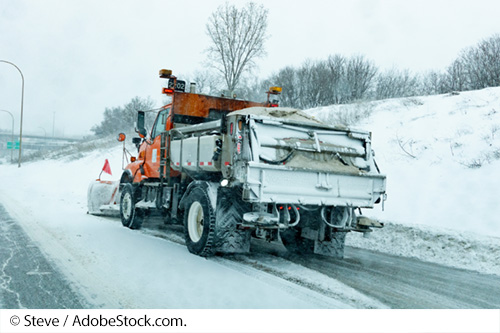 A dump truck with salt/gravel on a snow covered roadway. Image Source: © Steve / AdobeStock.com.