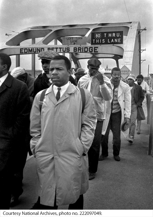 : A group of individuals on a bridge with a steel arch. Image Source: Courtesy National Archives, photo no. 222097049.