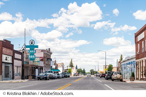 A small-town street is lined with cars and buildings. Image Source: © Kristina Blokhin / AdobeStock.com.