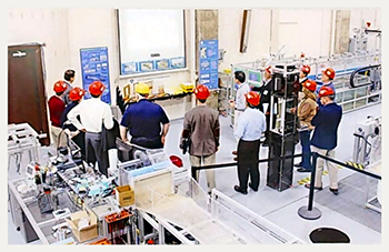 A group of people wearing hard hats gathers around a display in a room full of equipment.