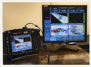 An ultrasonic controller sits next to a computer monitor showing various graphs and analytical information.