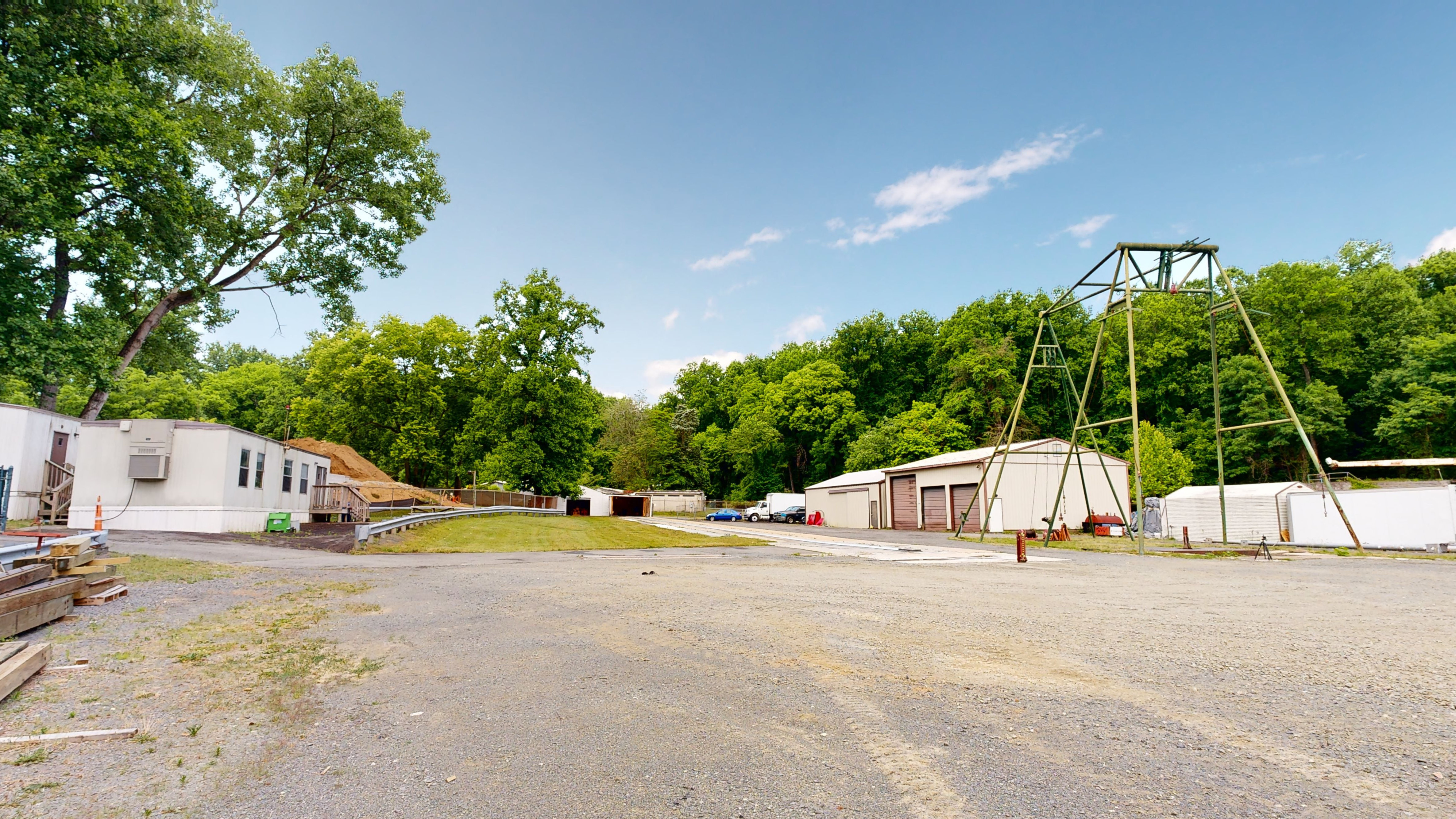 Outdoor testing area that has a long track, a runoff area, and several trailers and garages. Next to some of the garage buildings is a tall, A-framed scaffolding-type structure known as a pendulum tower, which is situated over a pendulum pit. 