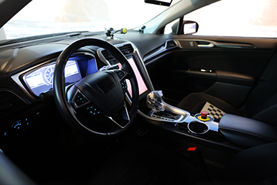 The interior of the driving simulator vehicle. The panel behind the steering wheel and in the center of the dashboard are inlaid with digital screens. 