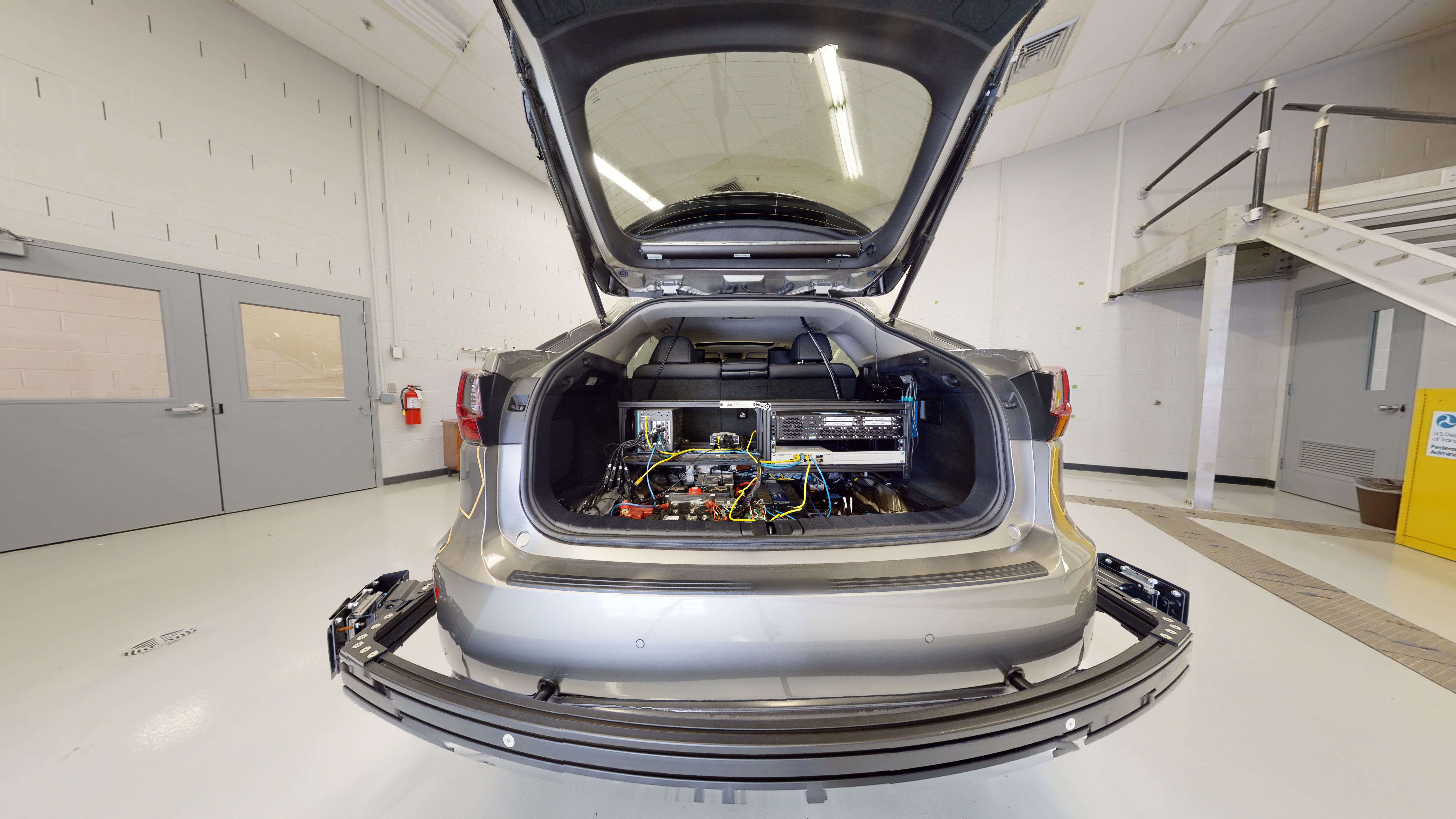 The open vehicle trunk shows equipment and wires to support self-driving functions. Additional equipment spans the length of the back bumper.