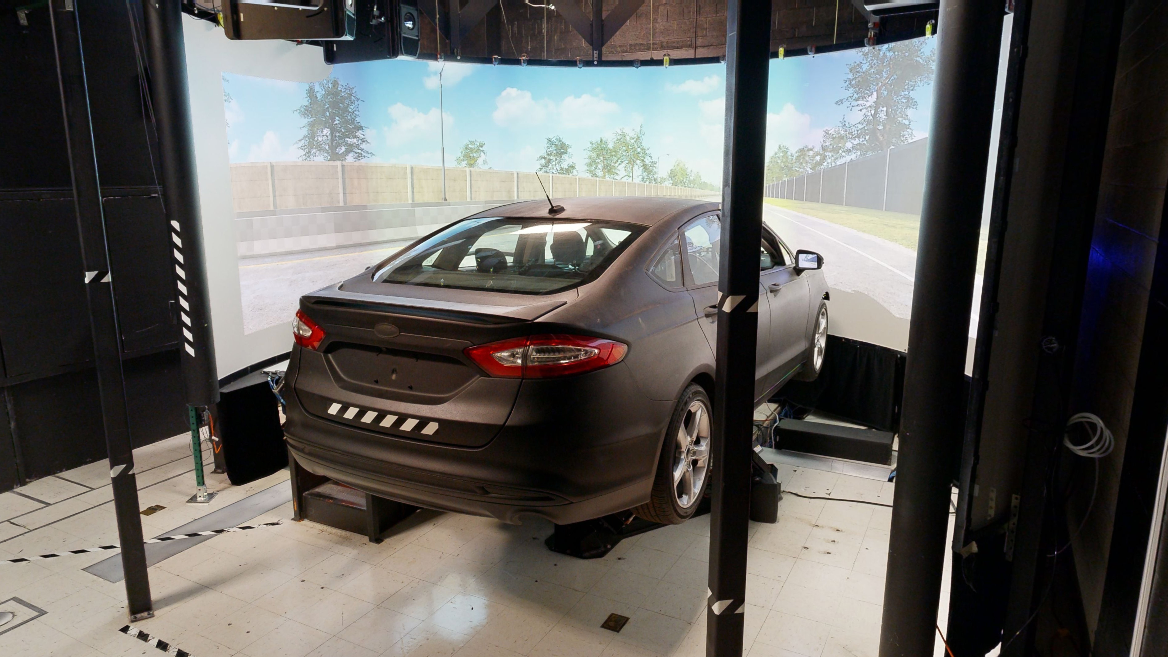 A sedan placed in front of a screen showing a simulated highway scene. 