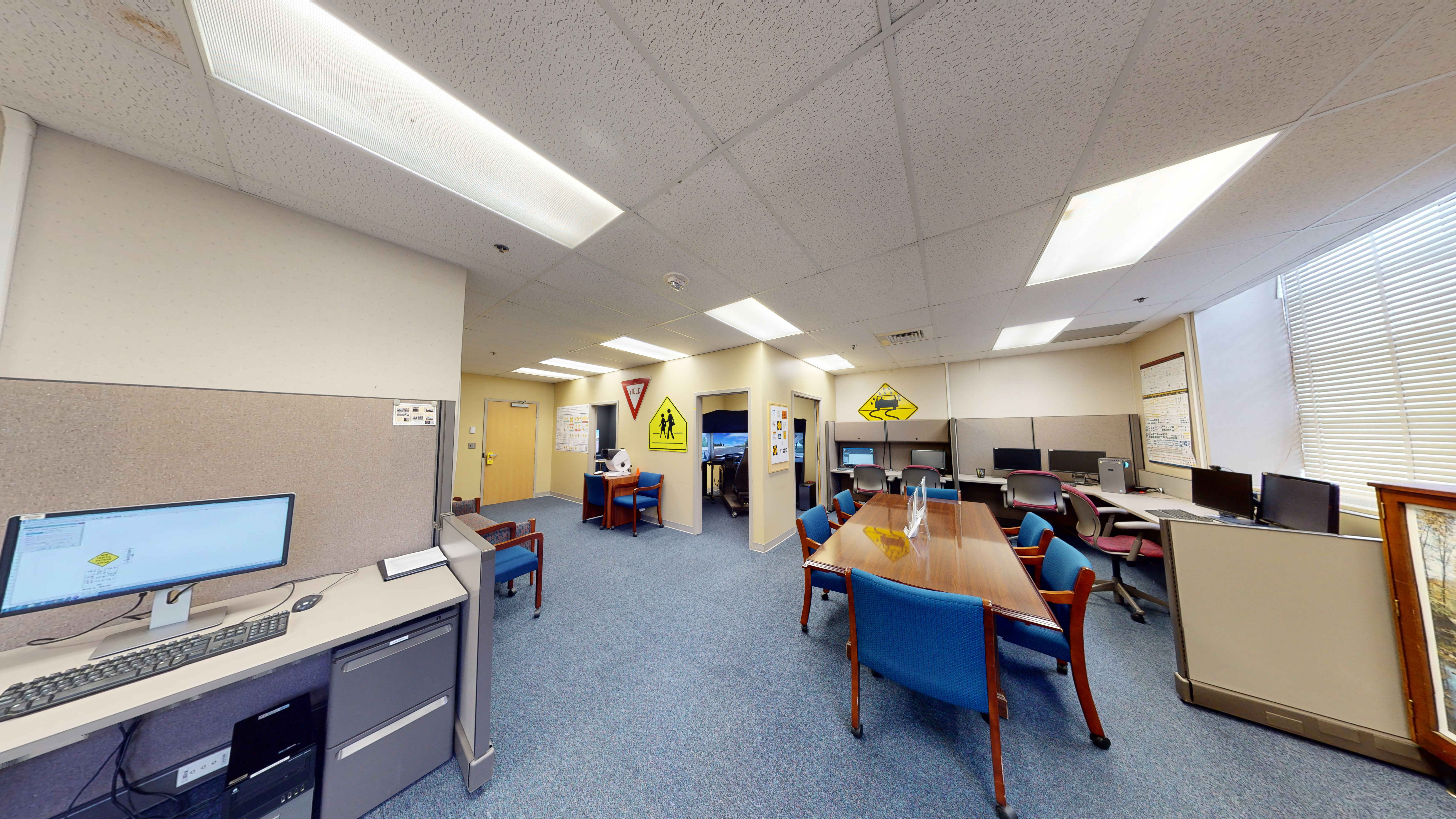 An office filled with desks, chairs, a long table, and computer monitors 