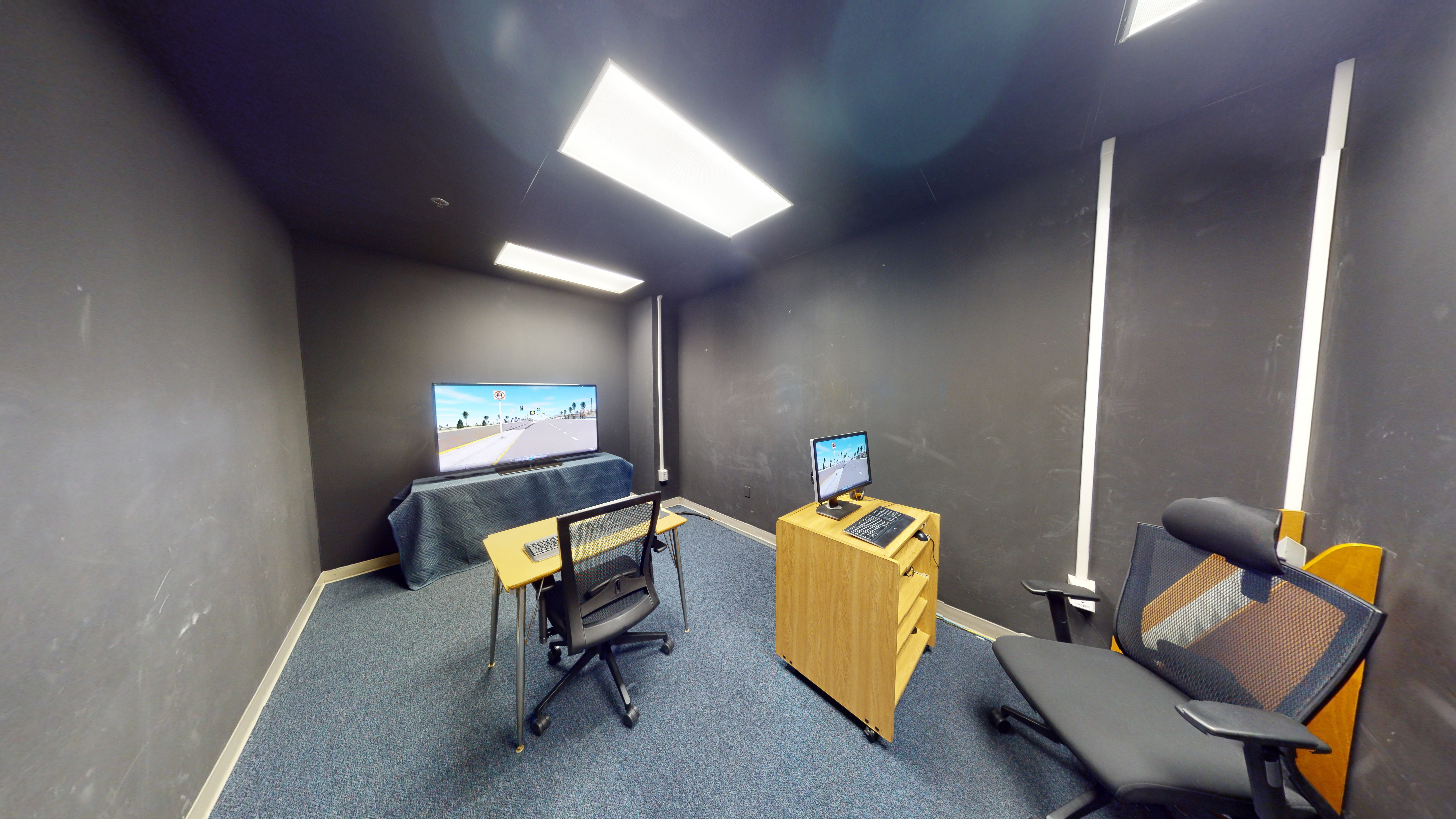 A room with a computer workstation, keyboards, and chairs facing a screen. 