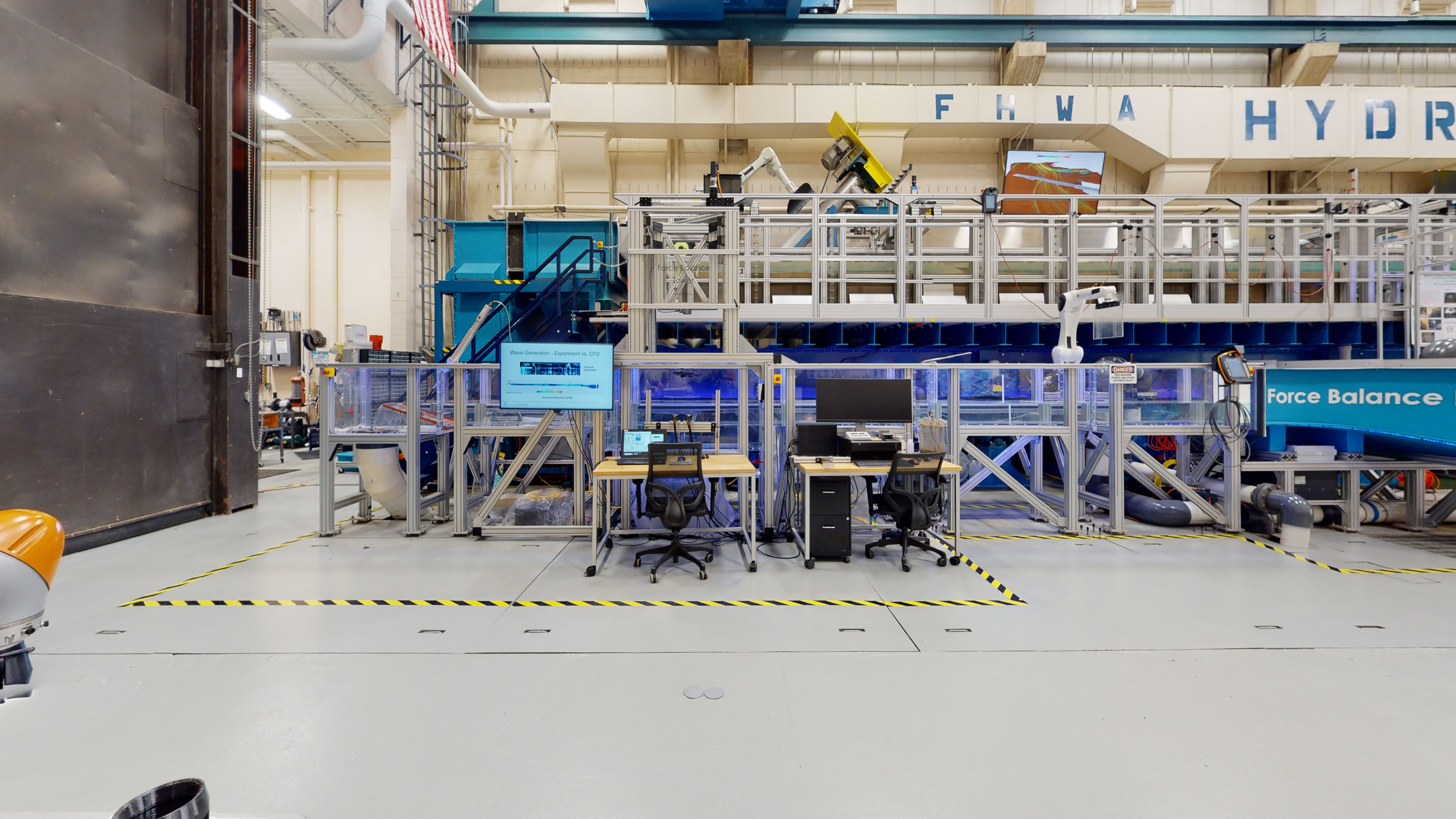 Part of a laboratory space with computer workstations, a stand-mounted monitor, and an automated robotic arm.  