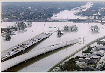 An aerial view of a flooded highway and surrounding areas. The roads disappear into the water, cutting off a significant portion of the highway. 