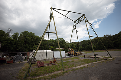 The scaffolding of a pendulum tower rises above a patch of grass surrounded by asphalt.  