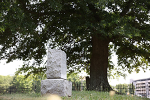 A stone headstone rises over a grassy area. 