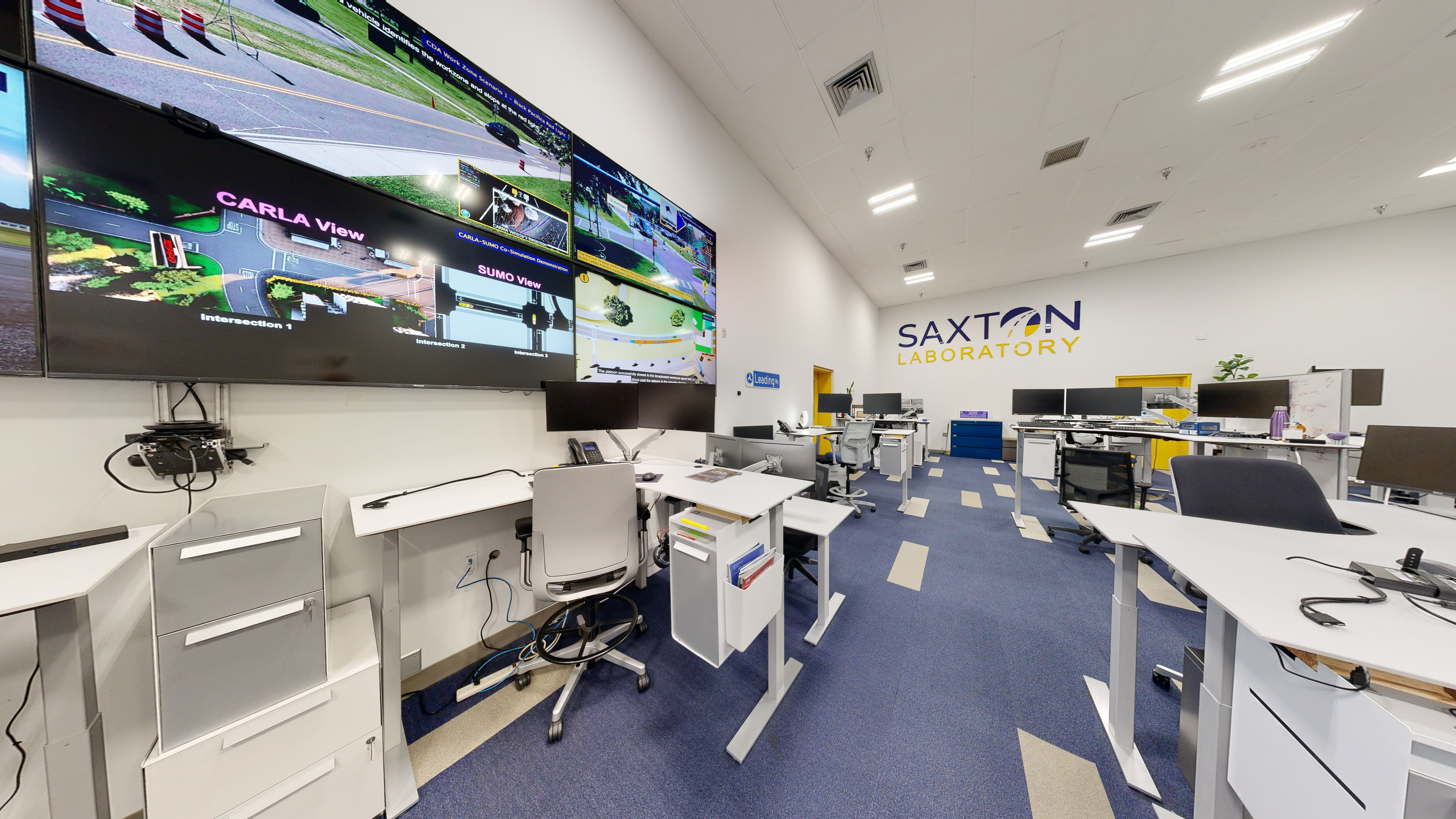 Office with several computer workstations and wall-mounted screens.