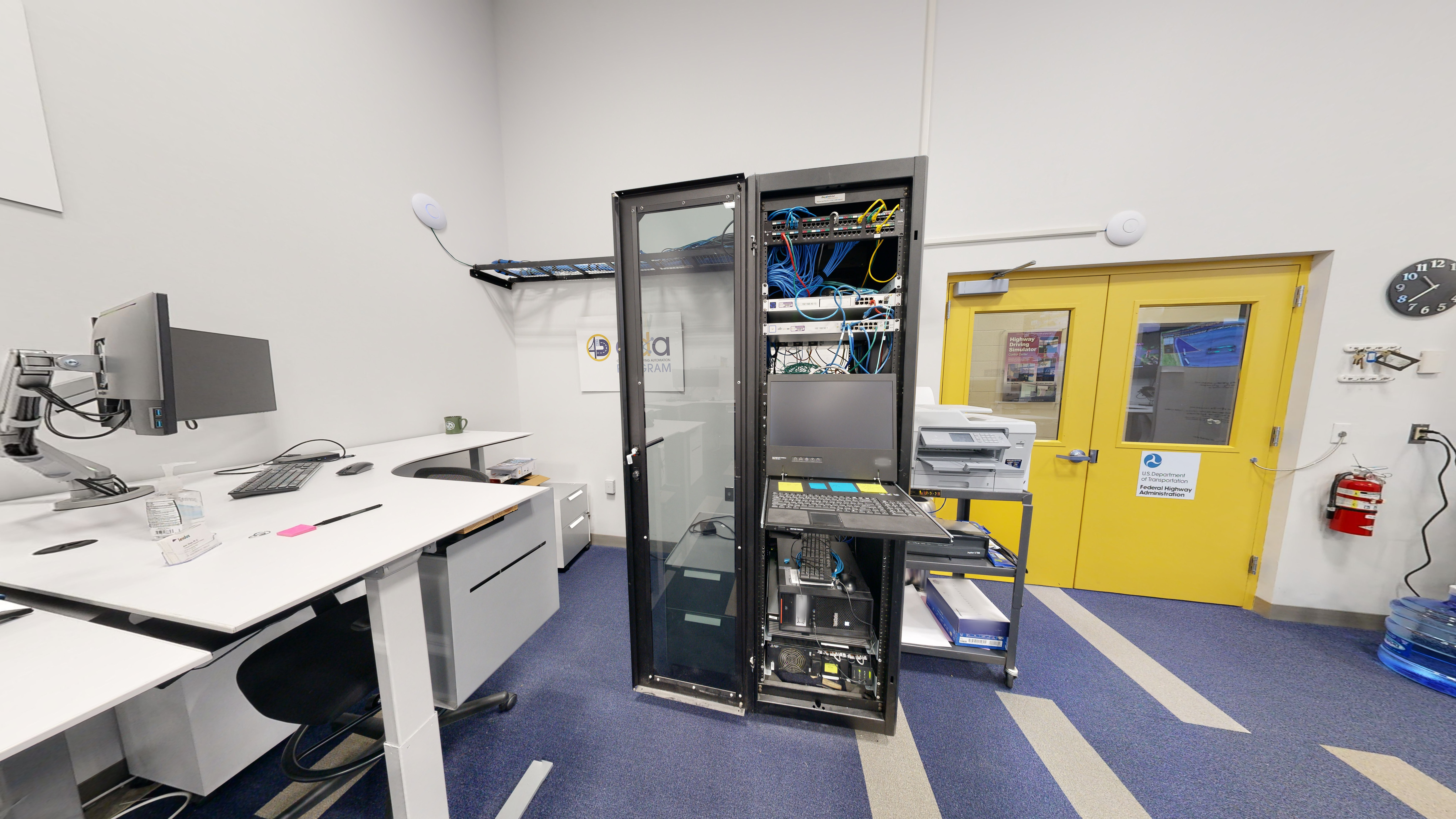 A tall media cabinet containing various controls, digital equipment, and a laptop. A printer is set up next to the cabinet on a rolling cart. 