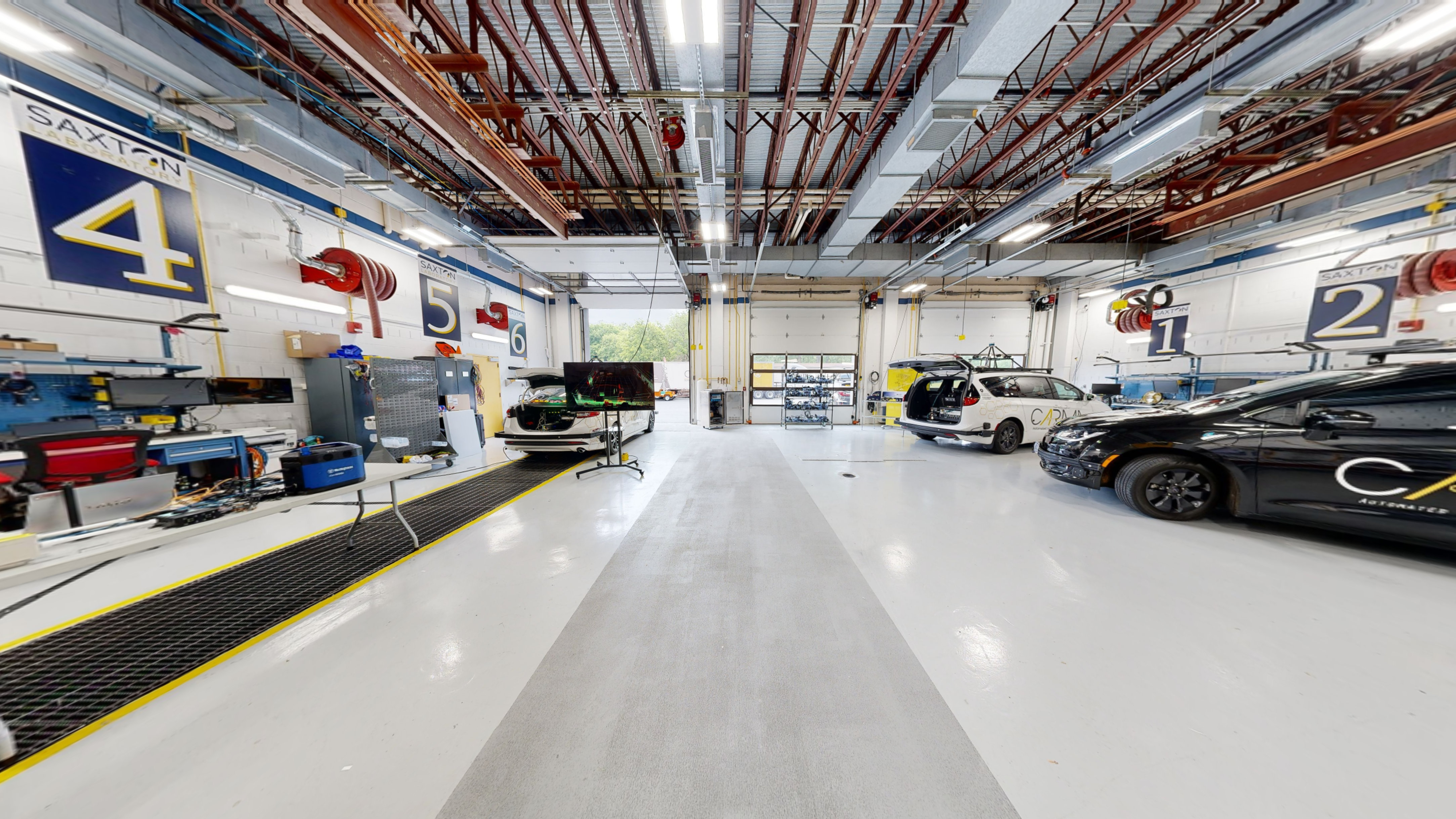 A three-doored garage area with various vehicles with equipment installed on top of their respective roofs that support self-driving functions.