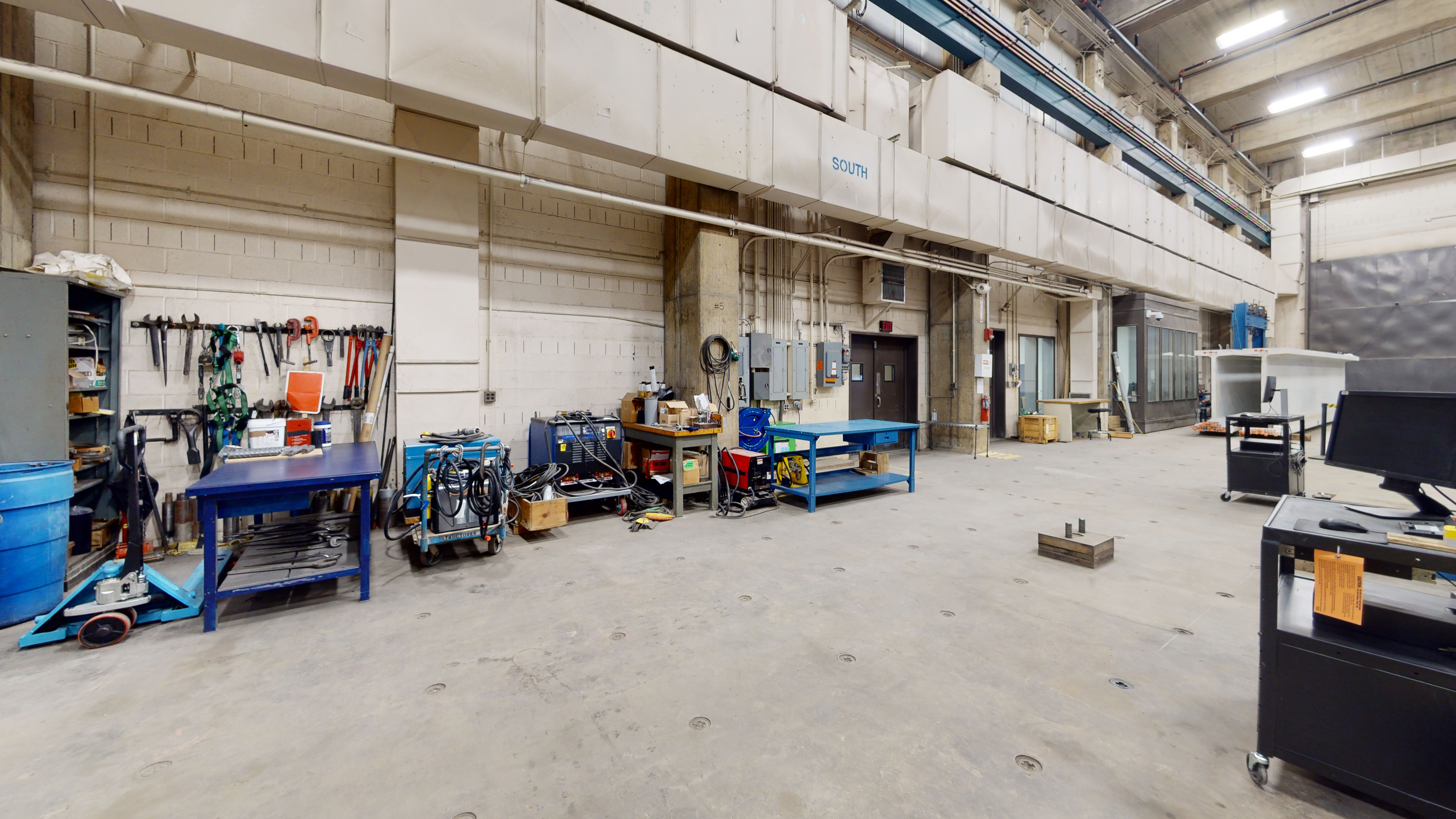 Part of a laboratory space filled with tables, equipment, tools, and machinery along the wall.  