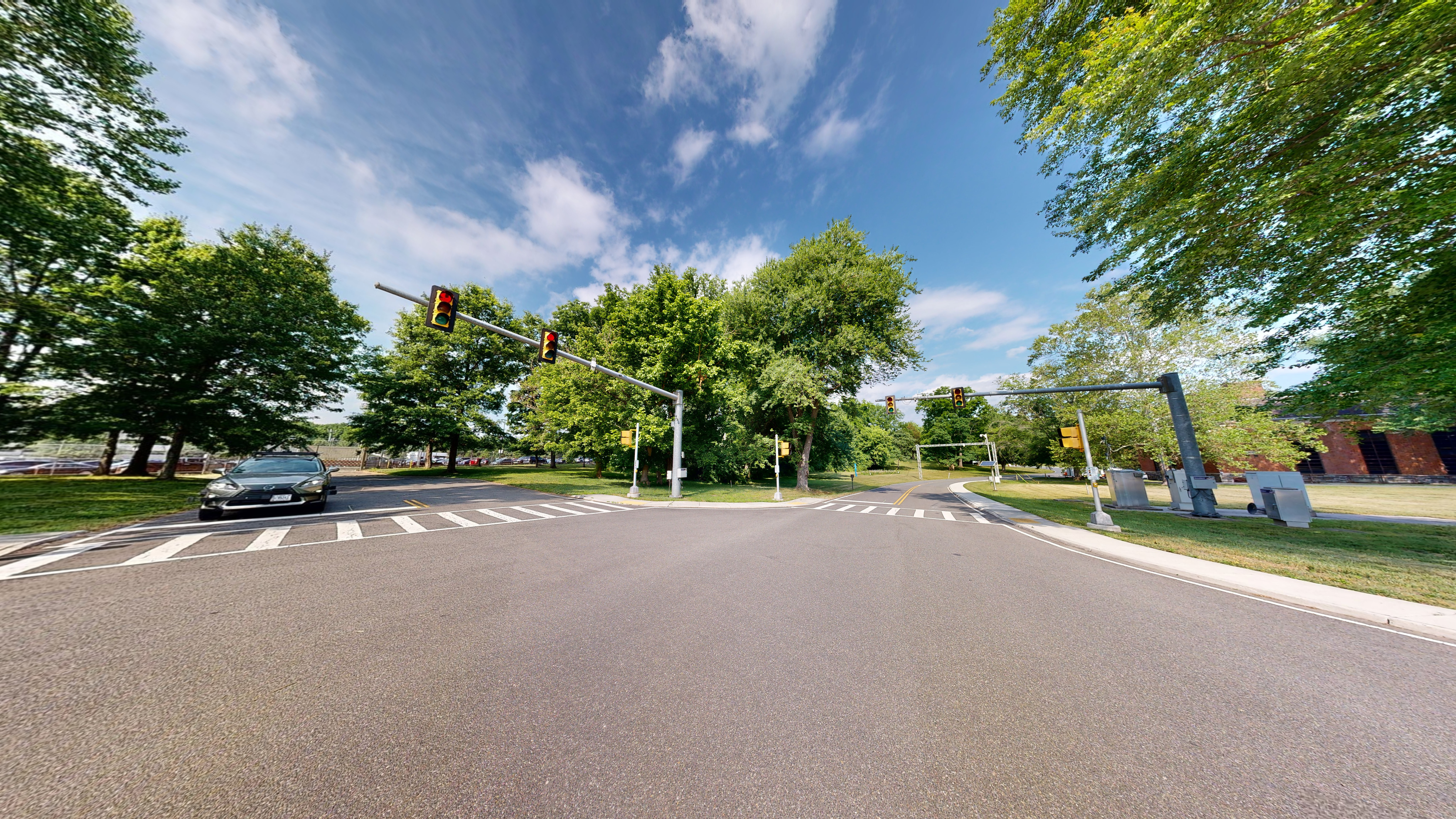 A street intersection with traffic and pedestrian walk signals on poles and crosswalks. A car is waiting at the intersection. 