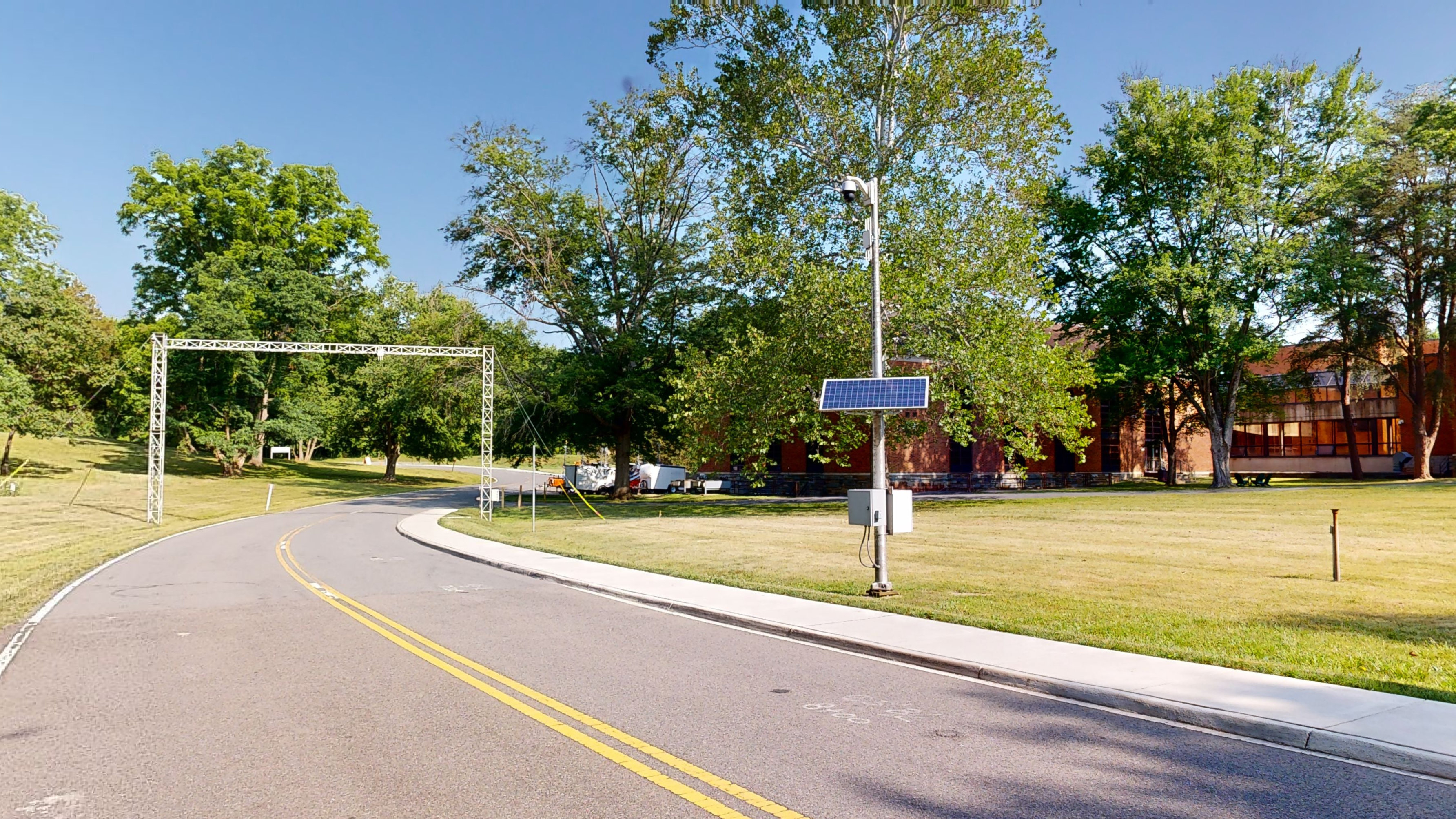 A street with a solar panel of a weather station on the right side and a structure that runs over it. 