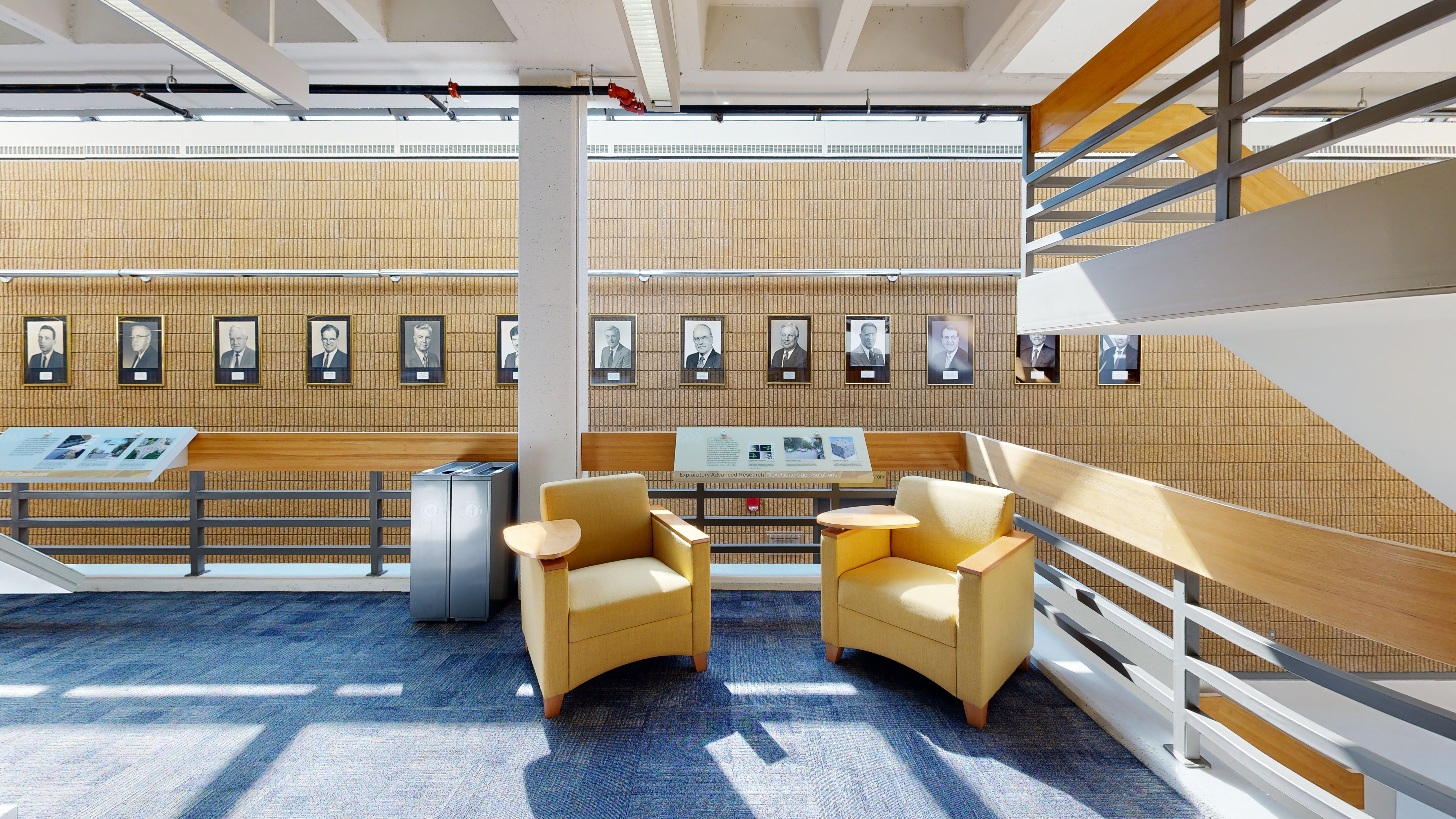 Seating area with chairs in front of informational signage and portraits lining the wall behind them.