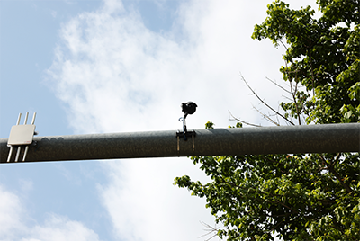 A thermal pedestrian camera is mounted to the horizontal arm of a traffic light pole. Another device can be seen on the same pole.