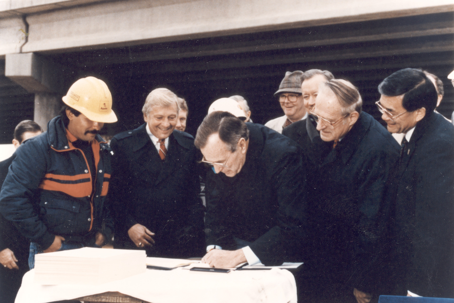 President George H.W. Bush signs ISTEA on Dec. 18, 1991, at a construction site in Texas. From left, construction worker Arnold Martinez, Rep. Bud Shuster, President Bush, Sen. Daniel Patrick Moynihan (in hat), Rep. John Paul Hammerschmidt, Rep. Robert Roe, and Rep. Norman Mineta.