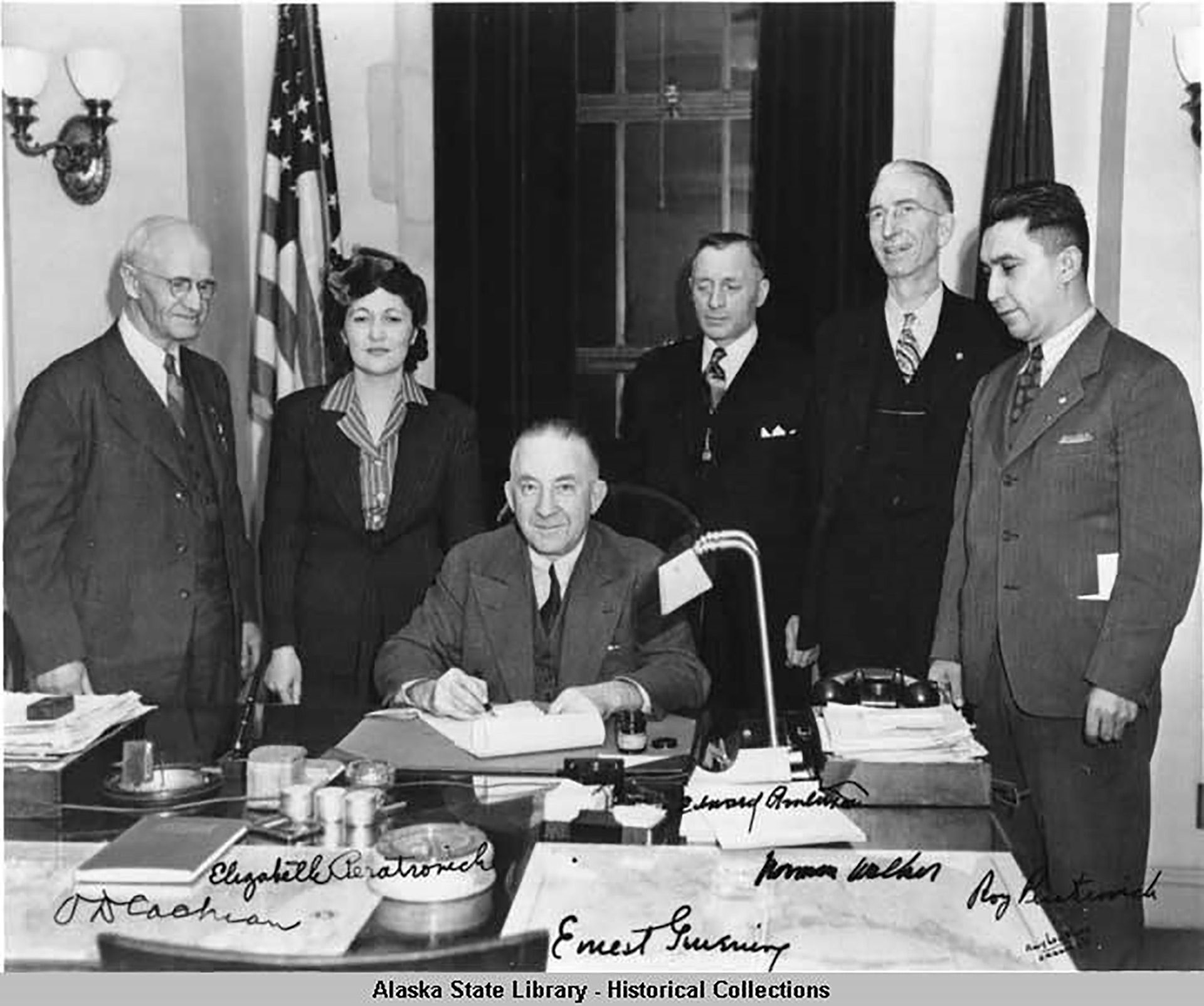 Governor Gruening (seated) signs the anti-discrimination act of 1945. Alaska Territorial Governors. Witnessing are (left to right) O. D. Cochran, Elizabeth Peratrovich, Edward Anderson, Norman Walker, and Roy Peratrovich. Image: Amy Lou Blood - Ordway's. 