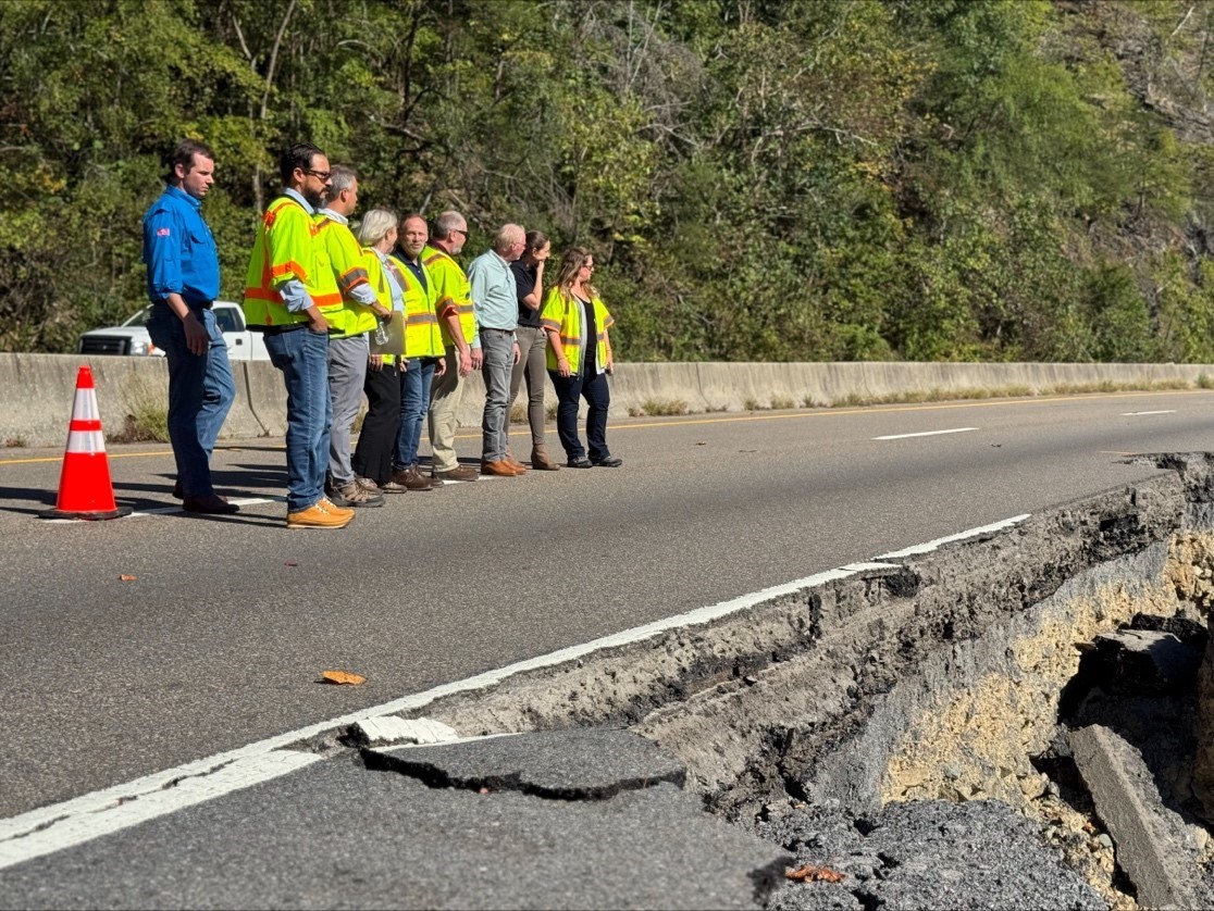 Kristin White and officials wearing yellow safety vests standing in a row on highway viewing damaged interstate