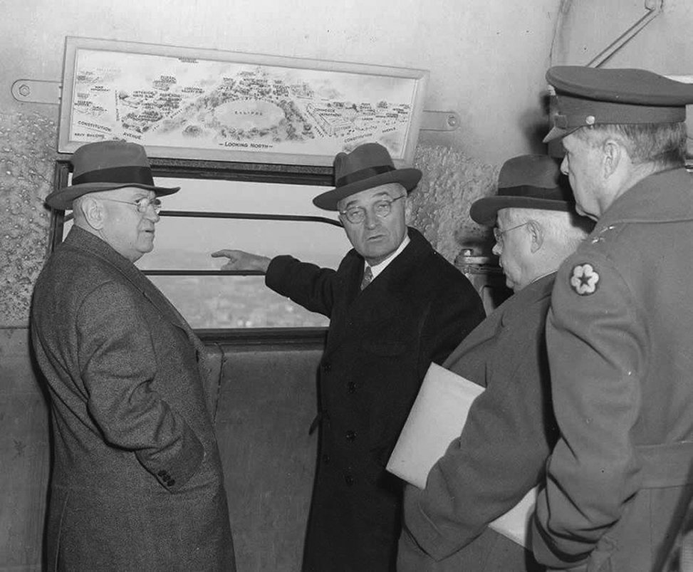 To decide whether the new bridge should include two four-lane spans or one six-lane span across the Potomac River, Secretary of the Interior Harold L. Ickles (left) invited President Harry S. Truman (gesturing at window) to the top of the Washington Monument on January 14, 1946. With them are Associate Director Arthur E. Demaray of the National Park Service and General Ulysses S. Grant III, chairman of NCP&PC the National Capital Park and Planning Commission, all single-bridge advocates. (Harry S. Truman Library)