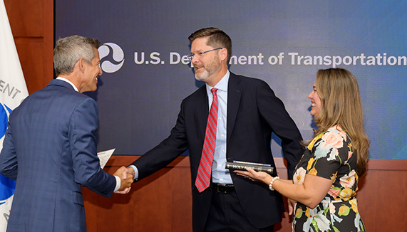 Sean McMaster shakes the hand of DOT Secretary Sean Duffy at his swearing-in. He is accompanied by his wife, who stood beside him.